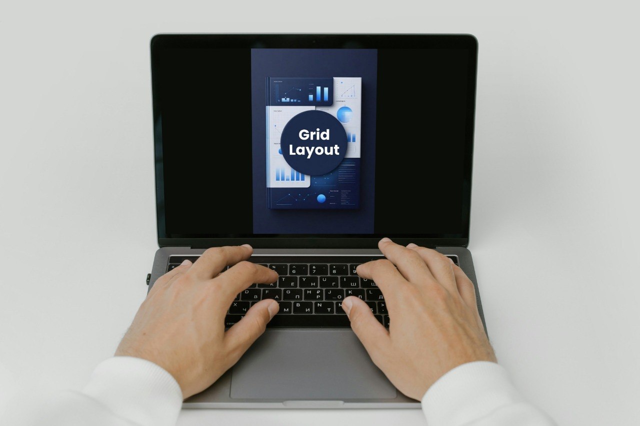 Person using a laptop with a screen displaying 'Grid Layout' on a white background
